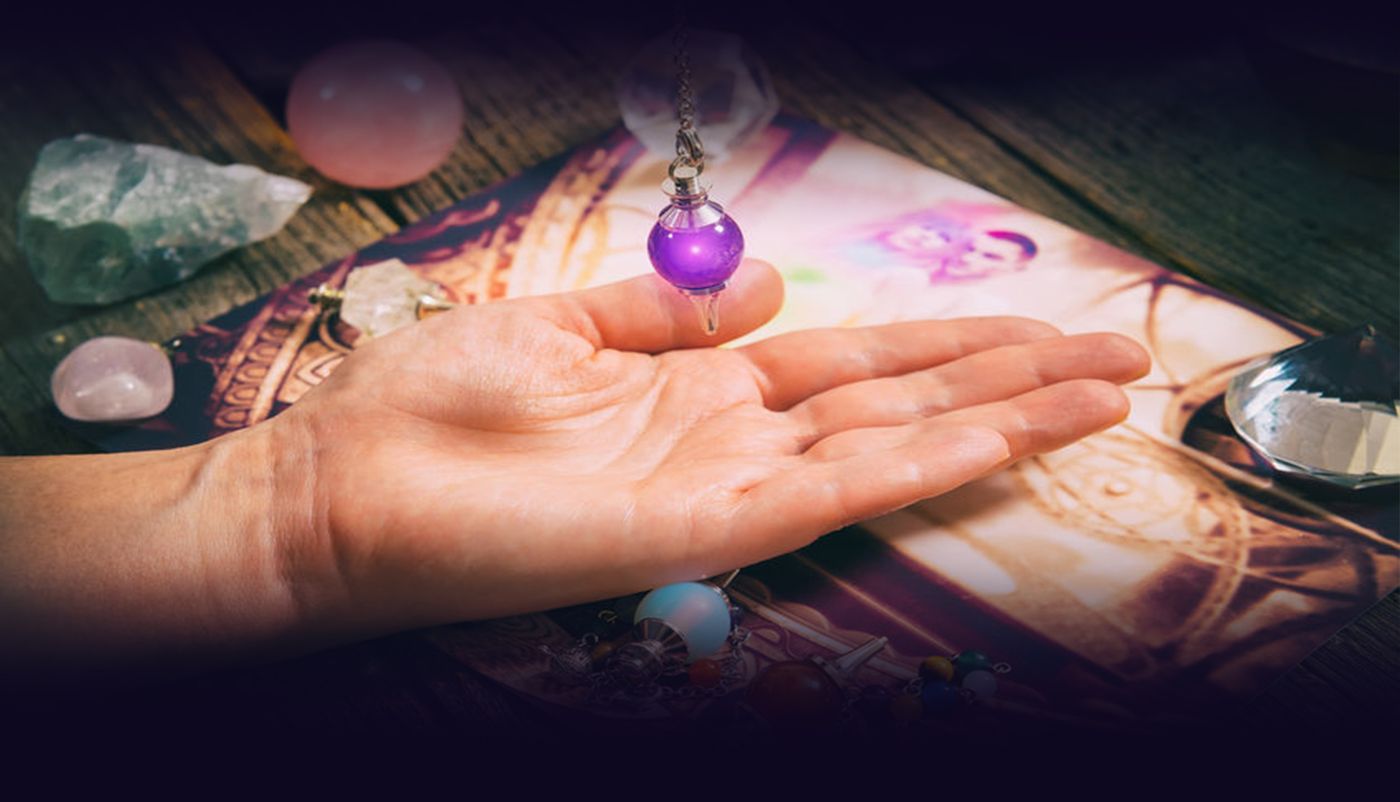 Hand met een pendel boven edelstenen op een doek